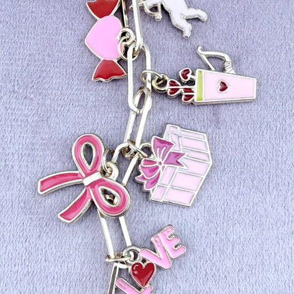 Valentine’s-themed charm keychain featuring pink and red enamel heart and love charms clipped to a phone case and displayed on a soft pink background.