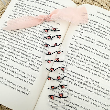 Clear acrylic Valentine’s Day bookmarks with pastel designs and soft chiffon ribbons resting inside open books, styled with a cozy, romantic bookish aesthetic.