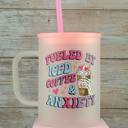 Pink tumbler with text 'Fueled by iced coffee & anxiety' on a wooden surface