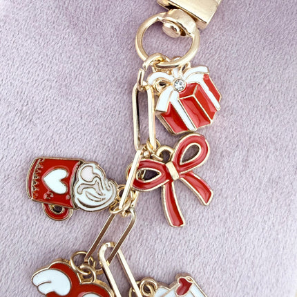 Valentine’s-themed charm keychain featuring pink and red enamel heart and love charms clipped to a phone case and displayed on a soft pink background.