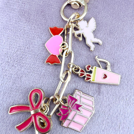 Valentine’s-themed charm keychain featuring pink and red enamel heart and love charms clipped to a phone case and displayed on a soft pink background.