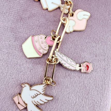 Valentine’s-themed charm keychain featuring pink and red enamel heart and love charms clipped to a phone case and displayed on a soft pink background.
