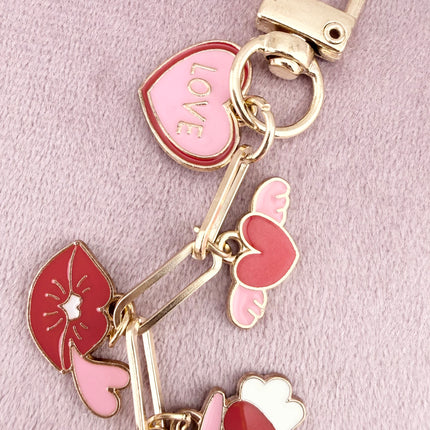 Valentine’s-themed charm keychain featuring pink and red enamel heart and love charms clipped to a phone case and displayed on a soft pink background.