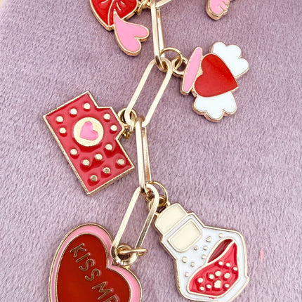 Valentine’s-themed charm keychain featuring pink and red enamel heart and love charms clipped to a phone case and displayed on a soft pink background.