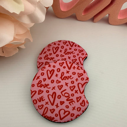 Two Valentine’s Day–themed neoprene car coasters with heart and love patterns, shown inside gift-ready packaging and styled on a neutral background.