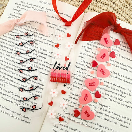 Clear acrylic Valentine’s Day bookmarks with pastel designs and soft chiffon ribbons resting inside open books, styled with a cozy, romantic bookish aesthetic.