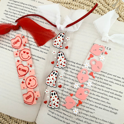 Clear acrylic Valentine’s Day bookmarks with pastel designs and soft chiffon ribbons resting inside open books, styled with a cozy, romantic bookish aesthetic.
