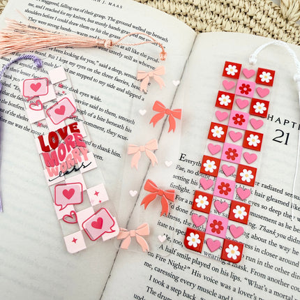 Handmade acrylic Valentine’s Day bookmarks featuring pink and red heart-themed designs with tassels, styled on open books for a cozy, festive reading aesthetic.