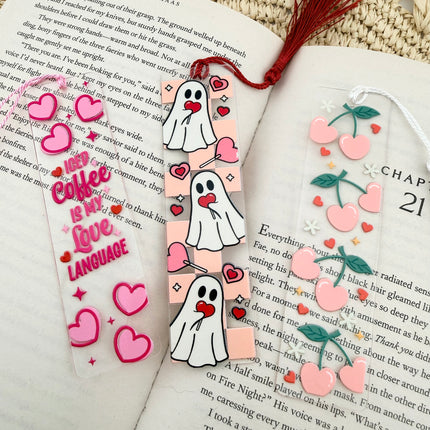 Handmade acrylic Valentine’s Day bookmarks featuring pink and red heart-themed designs with tassels, styled on open books for a cozy, festive reading aesthetic.