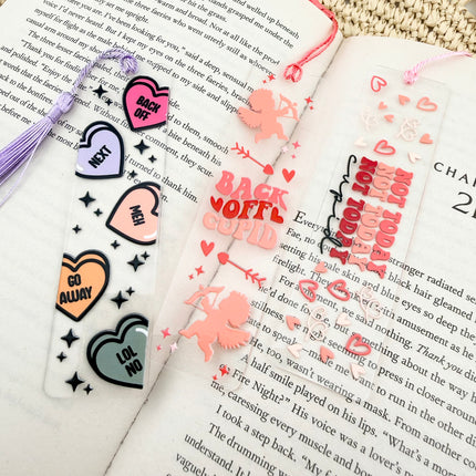 Handmade acrylic Valentine’s Day bookmarks featuring pink and red heart-themed designs with tassels, styled on open books for a cozy, festive reading aesthetic.