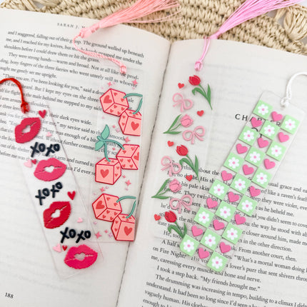 Handmade acrylic Valentine’s Day bookmarks featuring pink and red heart-themed designs with tassels, styled on open books for a cozy, festive reading aesthetic.