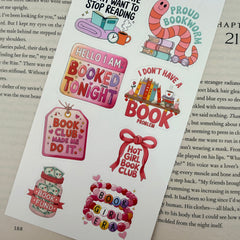Multiple book lover sticker sheet designs featuring cozy reading themes, spicy book humor, hearts, books, and playful illustrations displayed on an open book background.