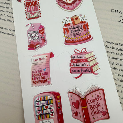 Valentine’s-themed bookish sticker sheets featuring pink and red hearts, books, cakes, and reading-inspired designs styled on an open book.