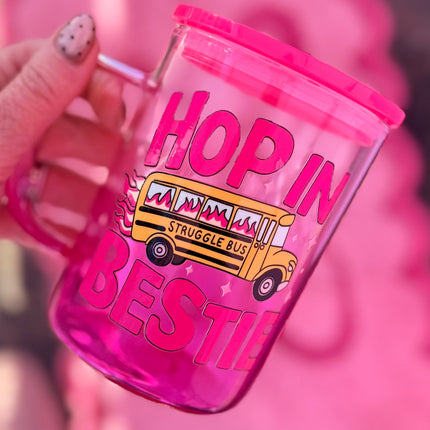 Pink tumbler with a school bus design and text held by a hand against a pink background