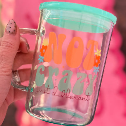 Clear mug with colorful text and a green lid held by a hand against a pink background