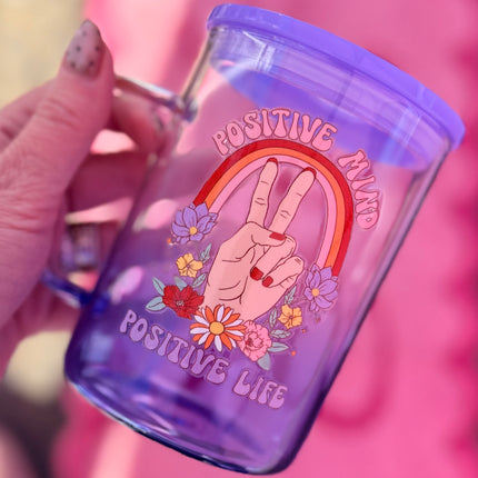 Purple tumbler with a peace sign, rainbow, and flowers design on a pink background