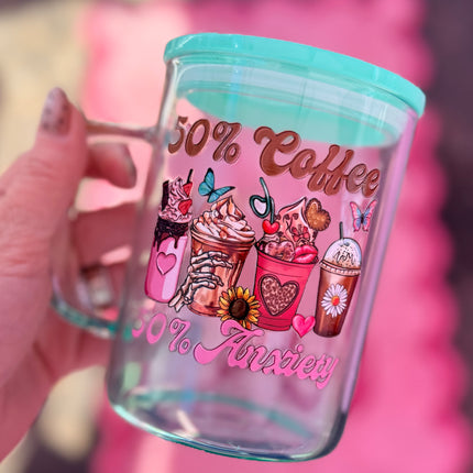 Glass tumbler with colorful coffee-themed design and text, held by a hand against a pink background.
