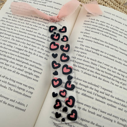 Clear acrylic Valentine’s Day bookmarks with pastel designs and soft chiffon ribbons resting inside open books, styled with a cozy, romantic bookish aesthetic.