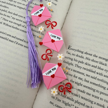 Handmade acrylic Valentine’s Day bookmarks featuring pink and red heart-themed designs with tassels, styled on open books for a cozy, festive reading aesthetic.