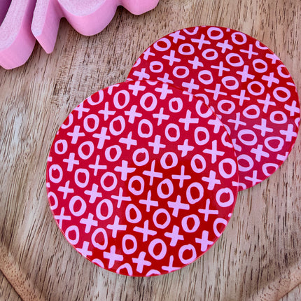 Round ceramic Valentine coasters featuring pink and red heart, bow, and XOXO designs, styled on a neutral surface and packaged ready to gift.