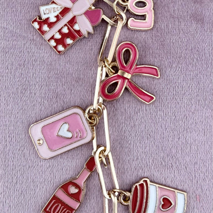 Valentine’s-themed charm keychain featuring pink and red enamel heart and love charms clipped to a phone case and displayed on a soft pink background.