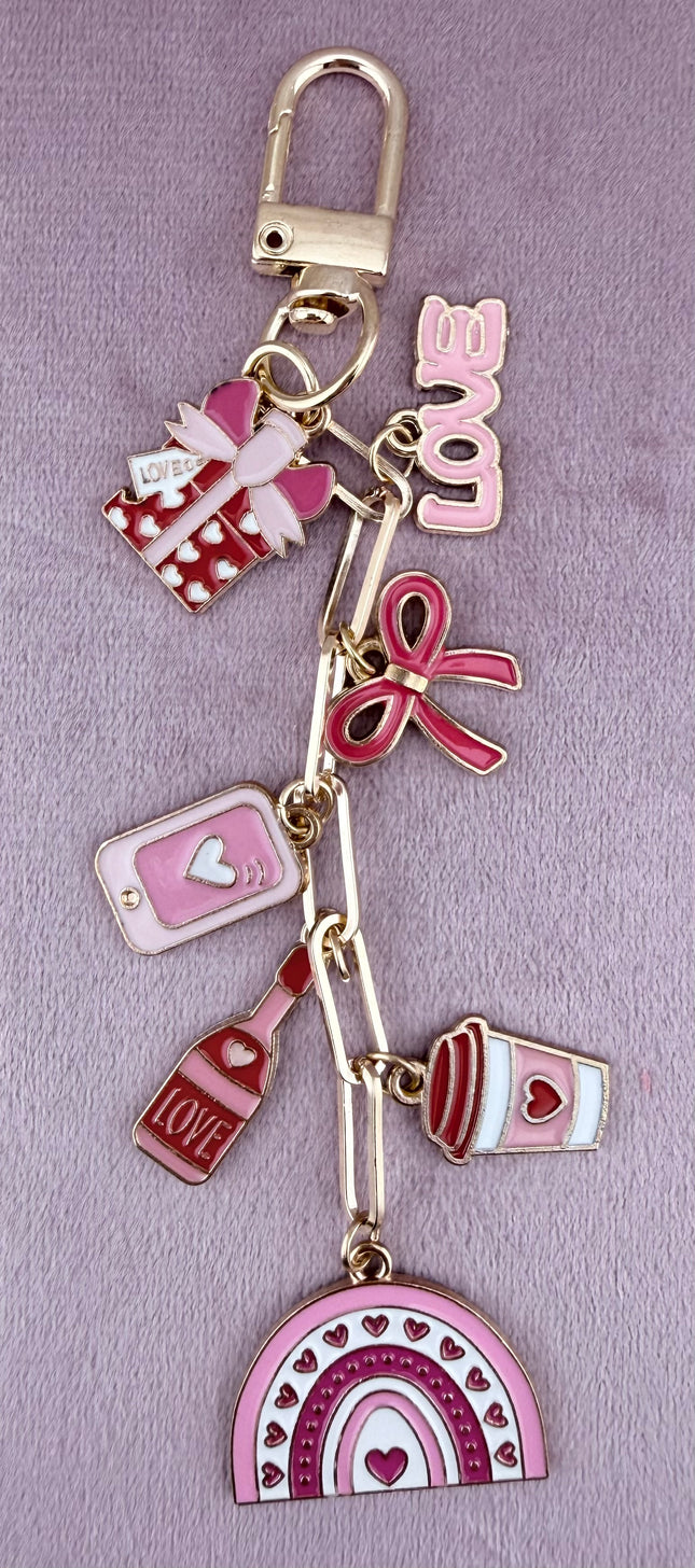 Valentine’s-themed charm keychain featuring pink and red enamel heart and love charms clipped to a phone case and displayed on a soft pink background.