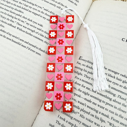 Handmade acrylic Valentine’s Day bookmarks featuring pink and red heart-themed designs with tassels, styled on open books for a cozy, festive reading aesthetic.