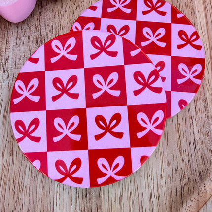 Round ceramic Valentine coasters featuring pink and red heart, bow, and XOXO designs, styled on a neutral surface and packaged ready to gift.