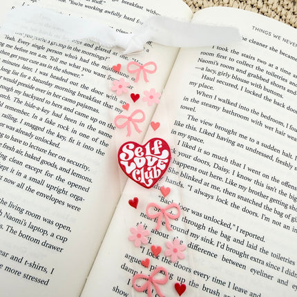 Clear acrylic Valentine’s Day bookmarks with pastel designs and soft chiffon ribbons resting inside open books, styled with a cozy, romantic bookish aesthetic.