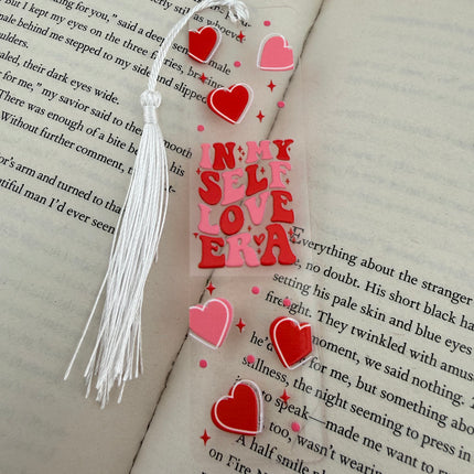 Handmade acrylic Valentine’s Day bookmarks featuring pink and red heart-themed designs with tassels, styled on open books for a cozy, festive reading aesthetic.