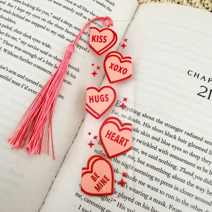 Handmade acrylic Valentine’s Day bookmarks featuring pink and red heart-themed designs with tassels, styled on open books for a cozy, festive reading aesthetic.