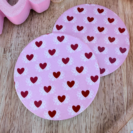 Round ceramic Valentine coasters featuring pink and red heart, bow, and XOXO designs, styled on a neutral surface and packaged ready to gift.