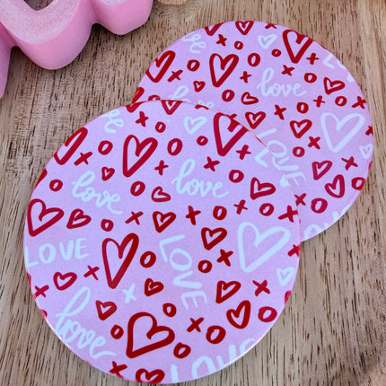 Round ceramic Valentine coasters featuring pink and red heart, bow, and XOXO designs, styled on a neutral surface and packaged ready to gift.