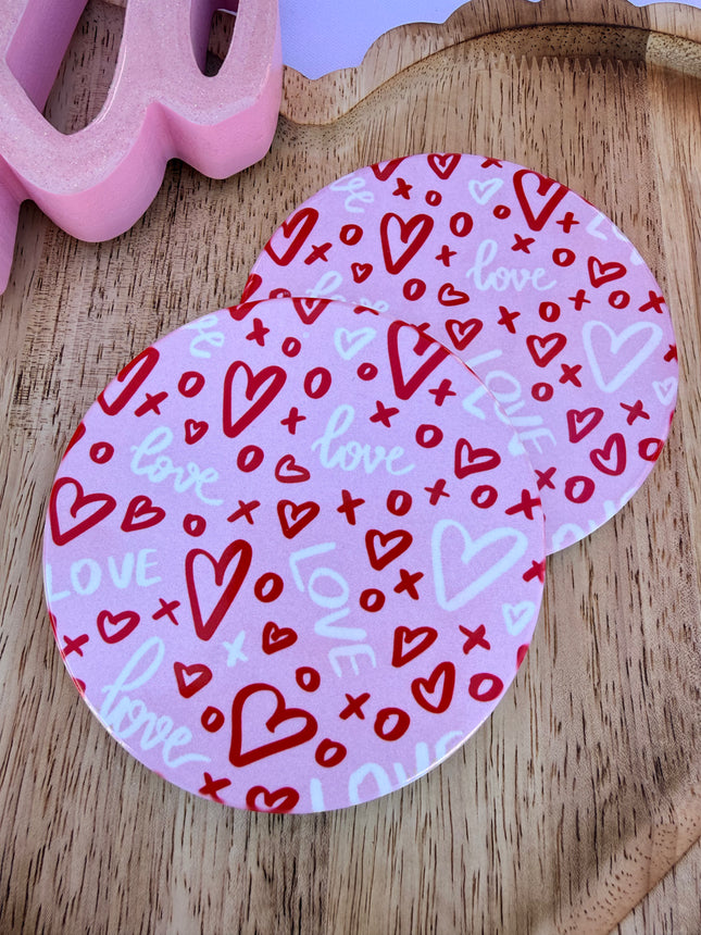 Round ceramic Valentine coasters featuring pink and red heart, bow, and XOXO designs, styled on a neutral surface and packaged ready to gift.
