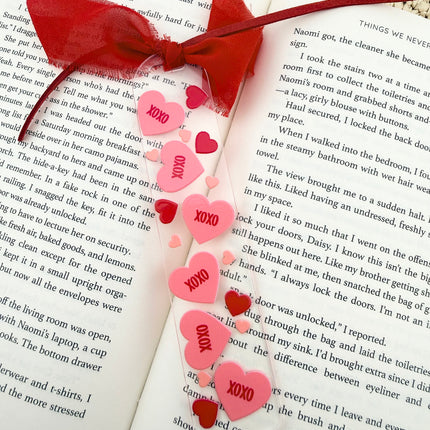 Clear acrylic Valentine’s Day bookmarks with pastel designs and soft chiffon ribbons resting inside open books, styled with a cozy, romantic bookish aesthetic.