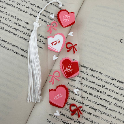 Handmade acrylic Valentine’s Day bookmarks featuring pink and red heart-themed designs with tassels, styled on open books for a cozy, festive reading aesthetic.