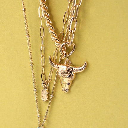 Gold plated three layer western style necklace featuring polished bull horn charm with elongated link chains and adjustable lobster claw clasp displayed on a feminine styled background.