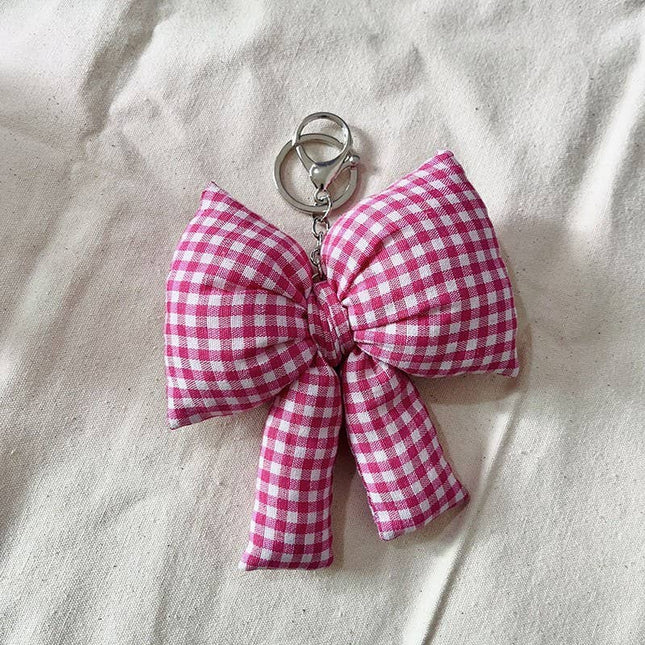 Pink gingham bow keychain on a beige fabric background