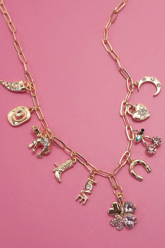 Gold western charm necklace featuring boots, cowboy hat, horseshoe, and heart charms styled on a pink background.