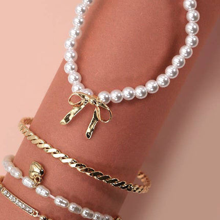 Set of 4 gold and pearl stretch bracelets with bow charm, rhinestone bar, and gold beading on soft green display.