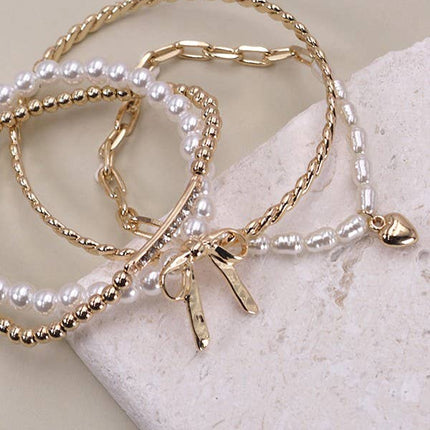 Set of 4 gold and pearl stretch bracelets with bow charm, rhinestone bar, and gold beading on soft green display.