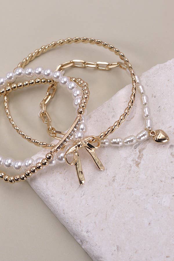 Set of 4 gold and pearl stretch bracelets with bow charm, rhinestone bar, and gold beading on soft green display.