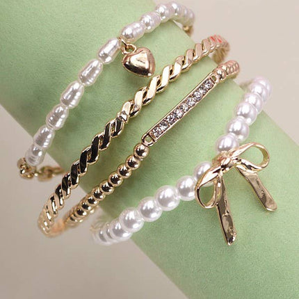 Set of 4 gold and pearl stretch bracelets with bow charm, rhinestone bar, and gold beading on soft green display.