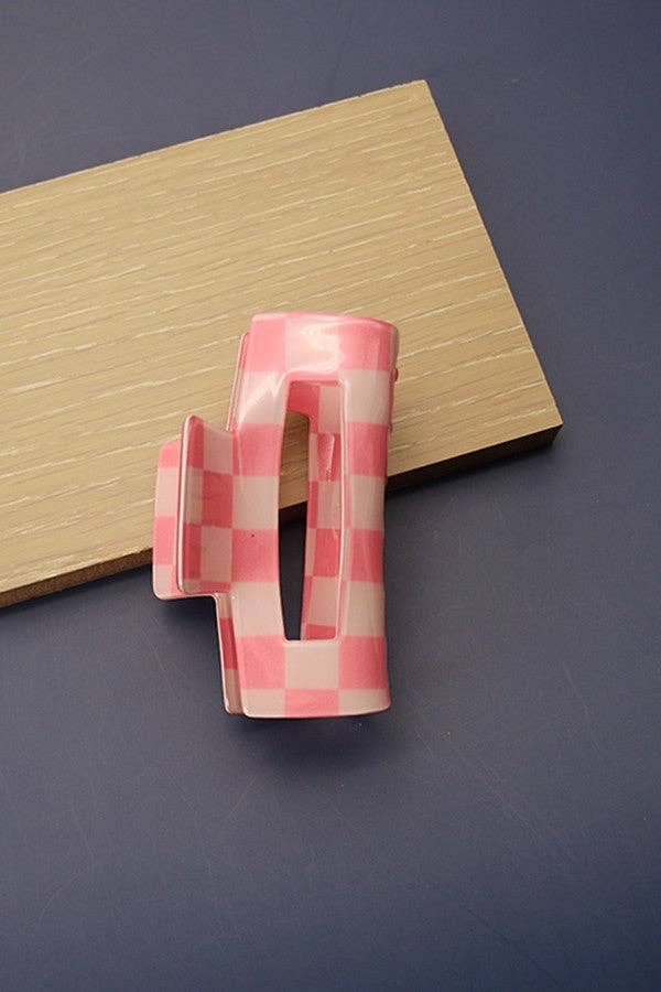 Pink and white checkered hair clip on a blue surface with a wooden block