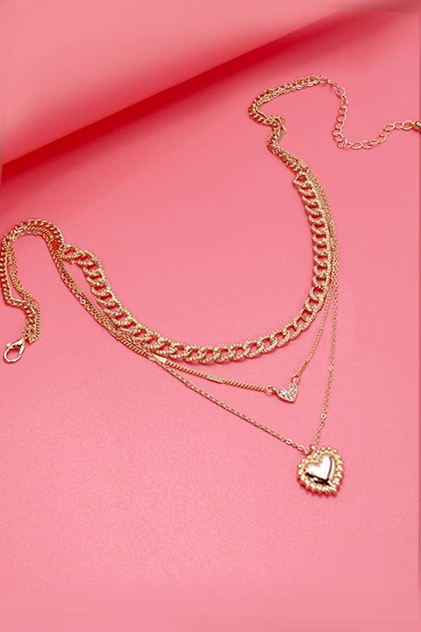 Gold layered necklace featuring multiple chains with rhinestone heart charms styled on a soft pink background.
