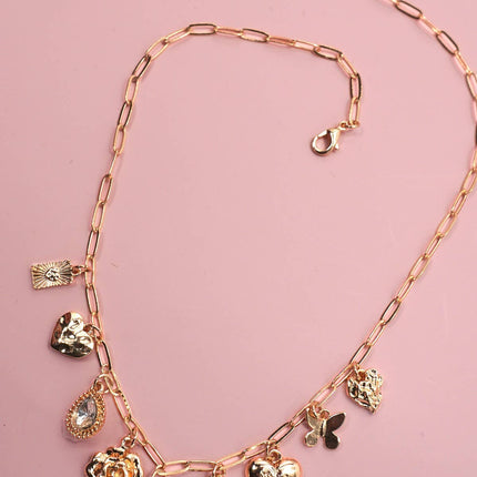 Gold necklace with various charms on a pink background