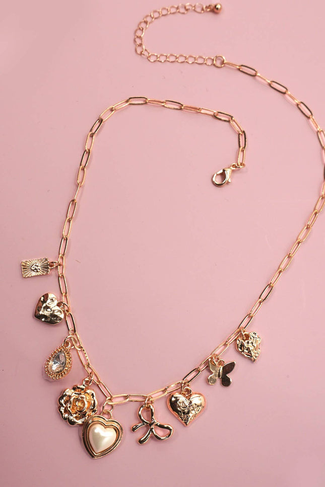 Gold necklace with various charms on a pink background