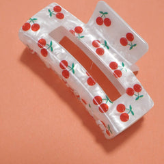 White hair clip with red cherry pattern on an orange background
