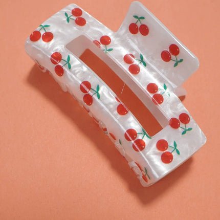 White hair clip with red cherry pattern on an orange background