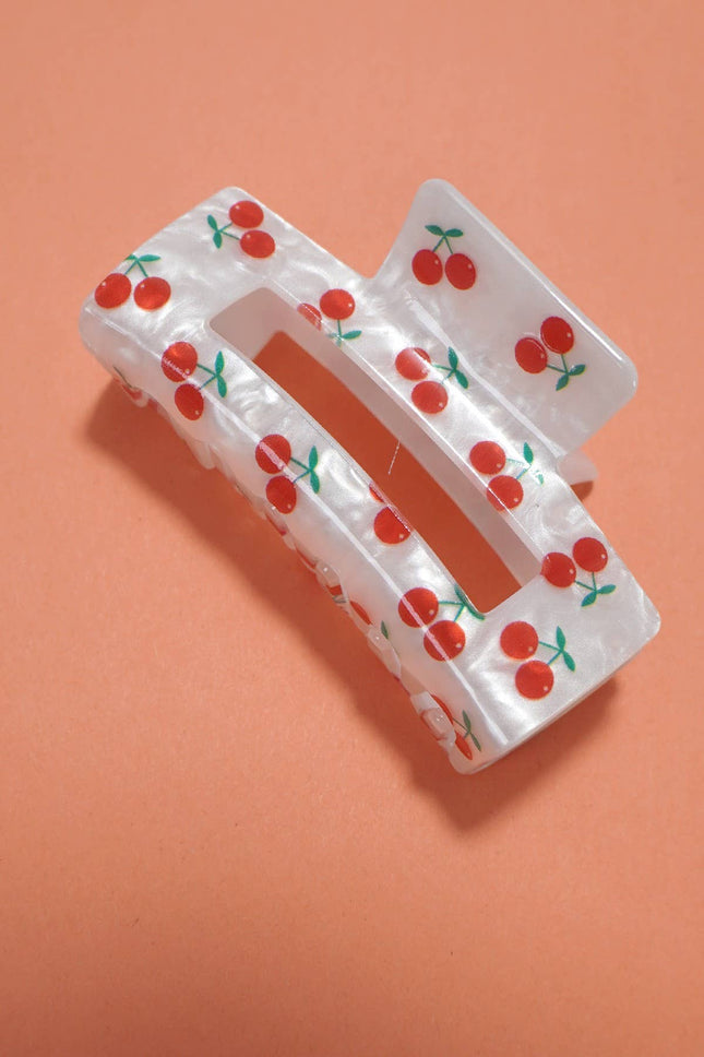 White hair clip with red cherry pattern on an orange background